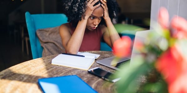 Exhausted female student feeling headache from problems with university course work connected to wifi for browsing informative websites, unhappy dark skinned woman tired from e learning on laptop